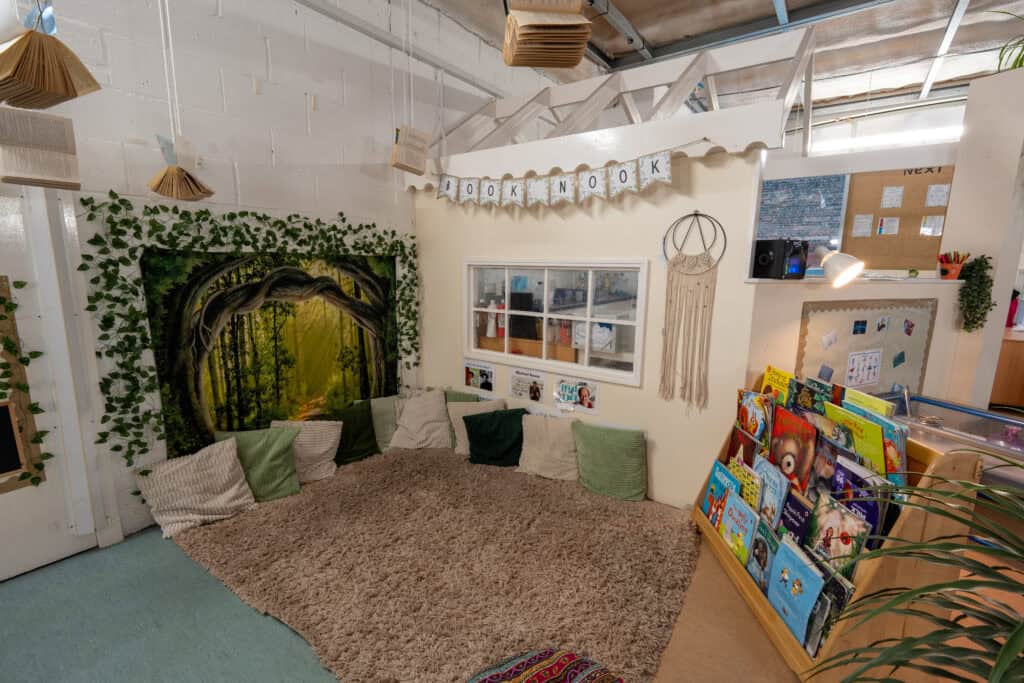 Bright and inviting nursery reading corner with forest-themed mural and soft seating.