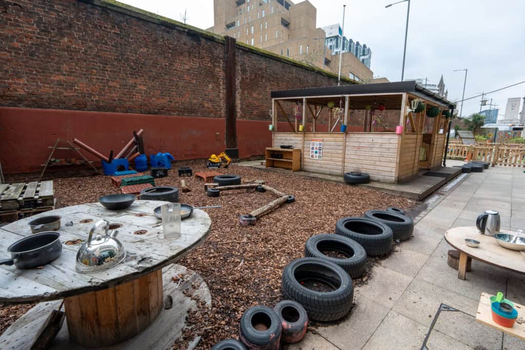Outdoor play area with tires, wooden structures, and sensory play equipment for children.