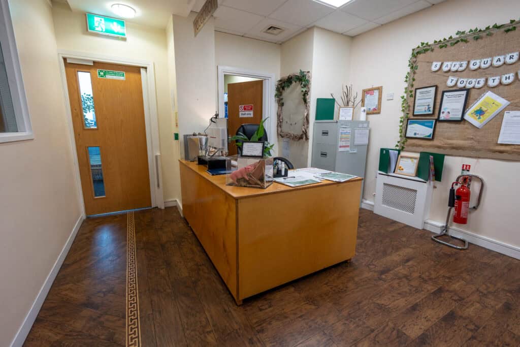 An inviting nursery reception with a wooden desk, informational displays, and safety equipment, creating a welcoming environment for children and parents at Thrive Childcare.
