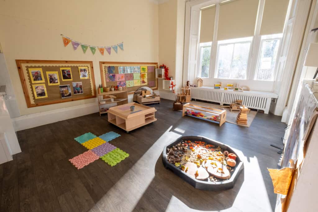 Bright indoor childcare playroom with toys, art displays, and natural sunlight, ideal for early childhood development and early learning at Thrive Childcare, fostering a safe, nurturing environment.