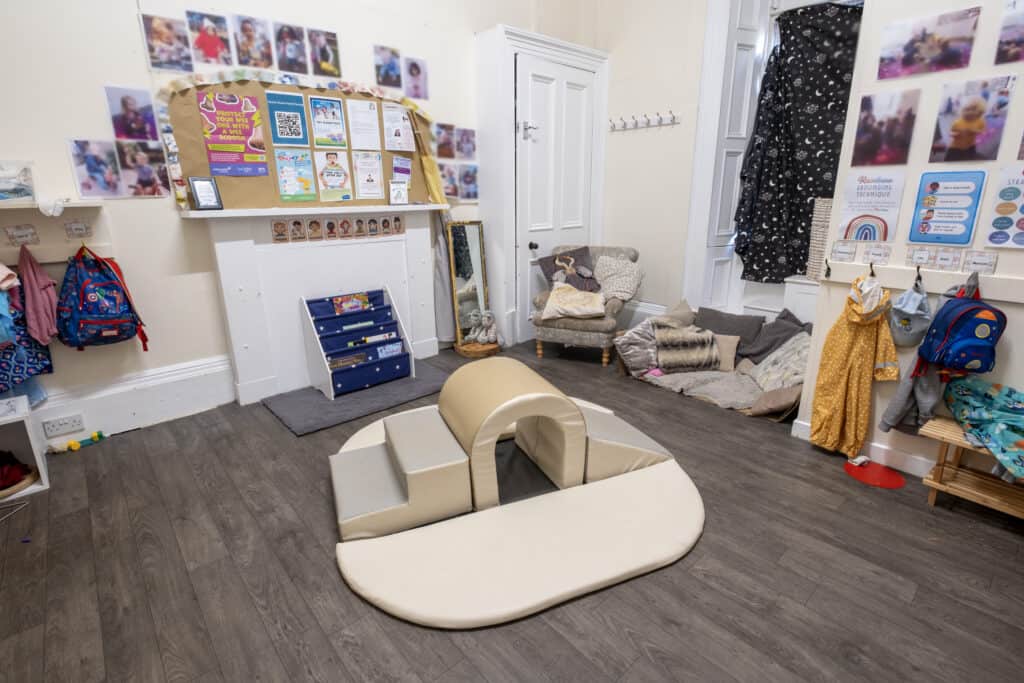 Bright childcare indoor play area at Thrive Childcare, featuring soft play equipment, educational posters, colourful backpacks, cosy reading nook, and engaging toddler activities, perfect for early childhood development.