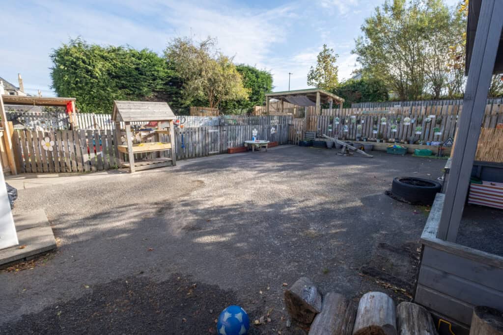 1. Childcare outdoor play area at Thrive Childcare, featuring safe fencing, play equipment, and garden space for early childhood development and outdoor activities.