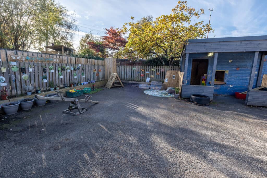A colourful, safe outdoor play area at Thrive Childcare with a wooden shed, play equipment, and garden decorations for toddler and preschool children's outdoor activities.