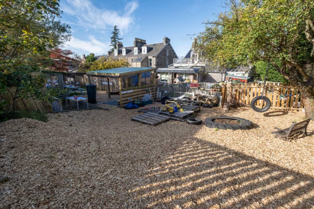 Playground outdoor area with wood chip flooring, toys, tire swings, and seating at Thrive Childcare in a charming residential neighbourhood. Perfect for children’s outdoor fun and learning.