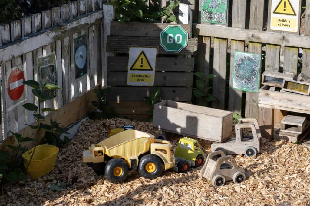 Bright children's wooden play area with toy trucks and construction signs, ideal for early learning and outdoor play at Thrive Childcare, promoting creative and safe play environments.