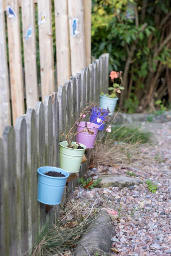 Colourful plant pots attached to a wooden fence outside Thrive Childcare, creating a welcoming garden space for children to explore nature and gardening activities.