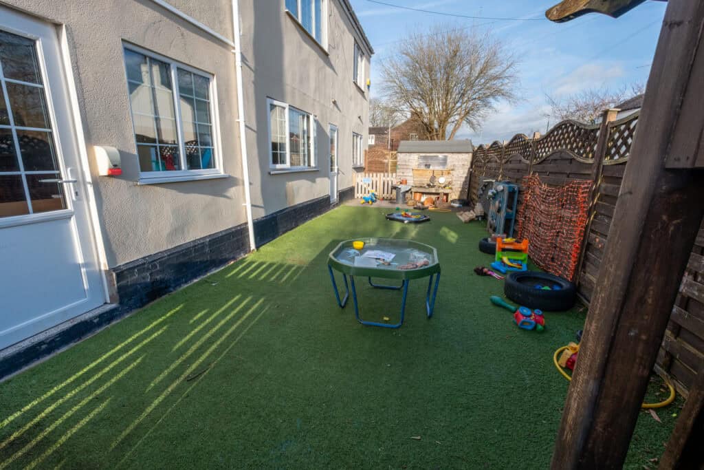 Outdoor childcare play area at Corner House Astbury with safe artificial grass and engaging toys for children.