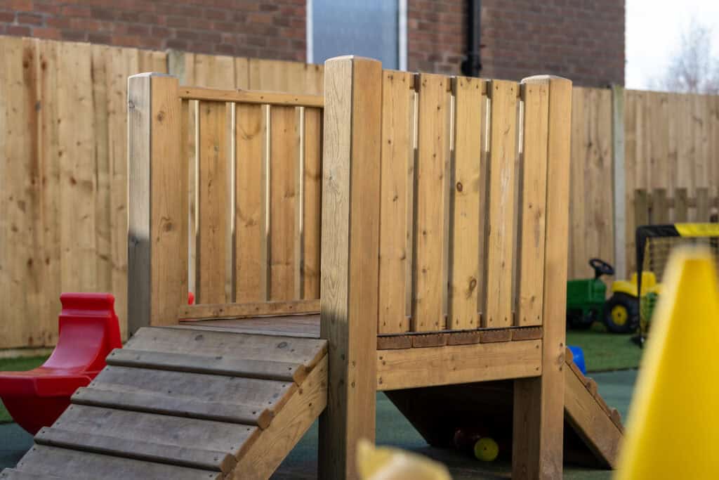 Bright wooden play structure with slide and climbing ramp at Corner House Astbury childcare centre. Safe outdoor space for children to enjoy active play and socialising.