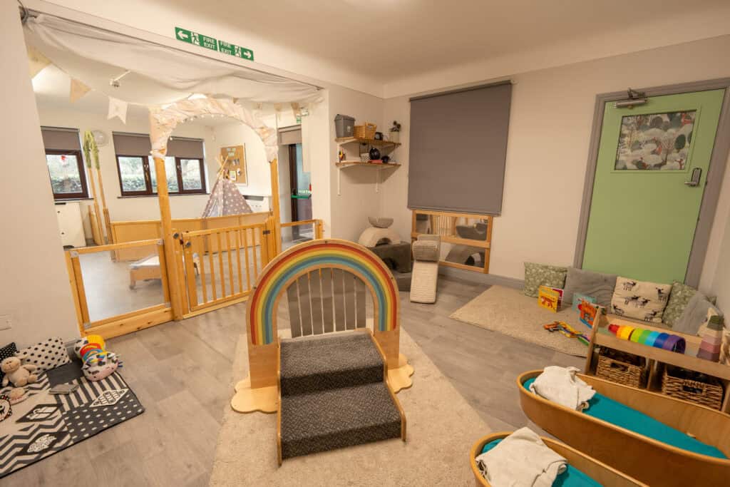 Bright and inviting indoor play area at Thrive Grosvenor House childcare centre, featuring soft mats, toys, and a rainbow-themed climbing structure for young children.