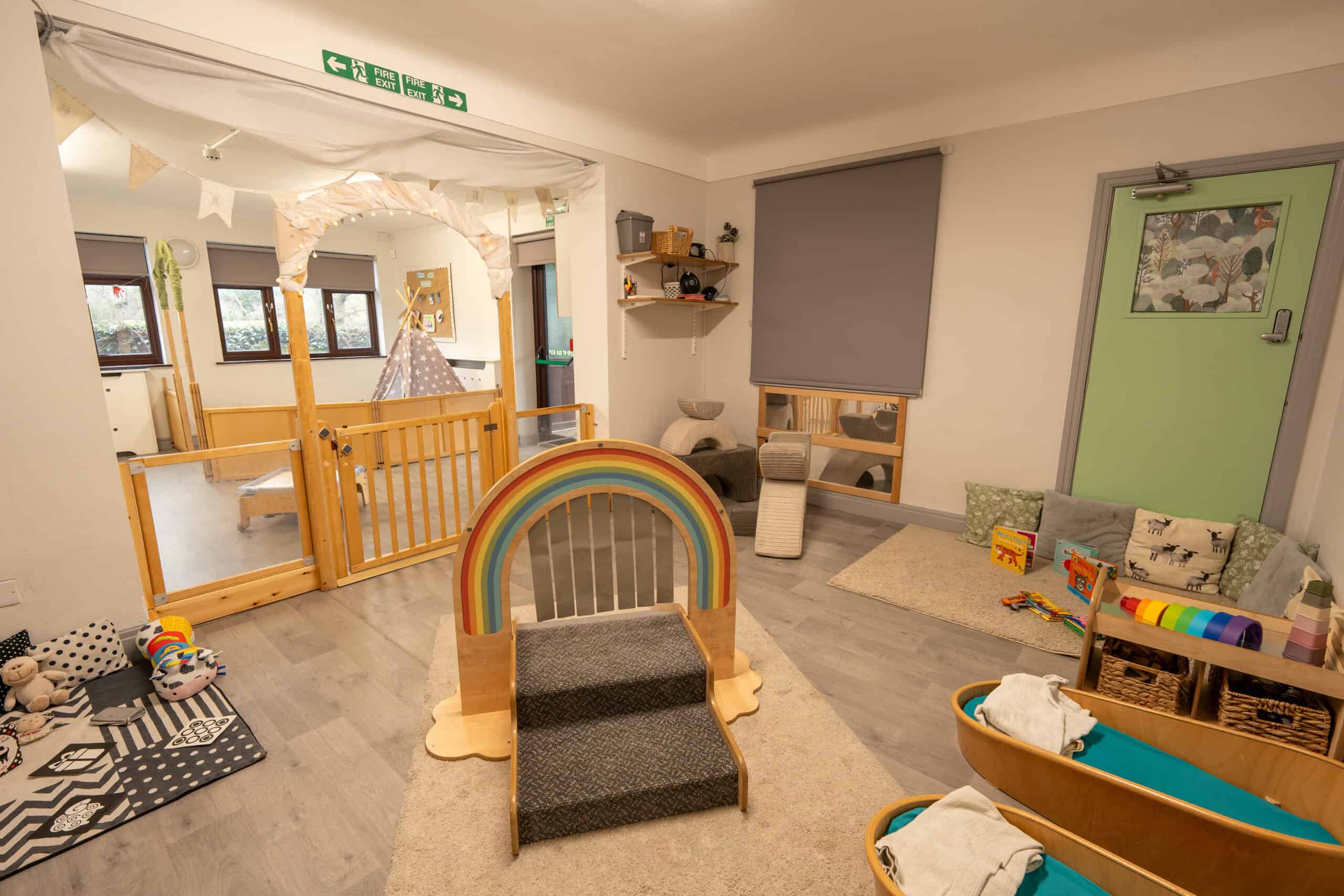 Bright and inviting indoor play area at Thrive Grosvenor House childcare centre, featuring soft mats, toys, and a rainbow-themed climbing structure for young children.