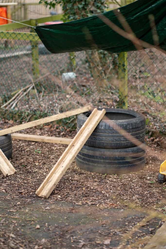Outdoor play area with tires, wooden planks, and a green tarp, part of Thrive Grosvenor House childcare setting.