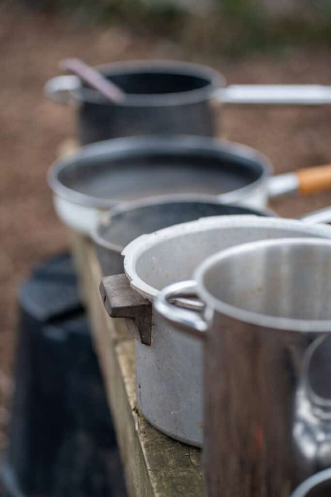 Outdoor cooking pots on a wooden table, ready for a family or group meal in a childcare outdoor setting.