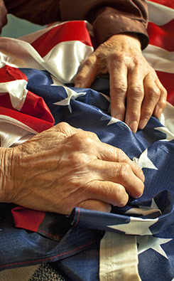 Elderly hands resting on a folded American flag, symbolizing veteran appreciation and legal support for seniors.