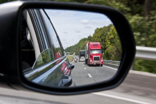 Semi-truck driving on highway viewed through car side mirror, transportation, highway safety, traffic accident legal advice, car accident attorney, Tuley Law Office.