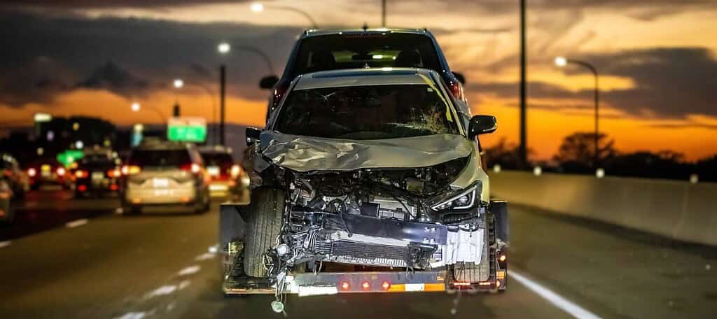 Car accident recovery on highway at dusk, tow truck transporting damaged vehicle for legal and insurance claims, professional car accident legal services by Tuley Law Office in Texas, accident attorneys.