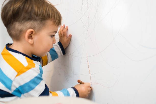 Baby Boy Writing on the white wall in his room with crayons - Upstairs Downstairs Cleaning Service kid marking flat paint walls