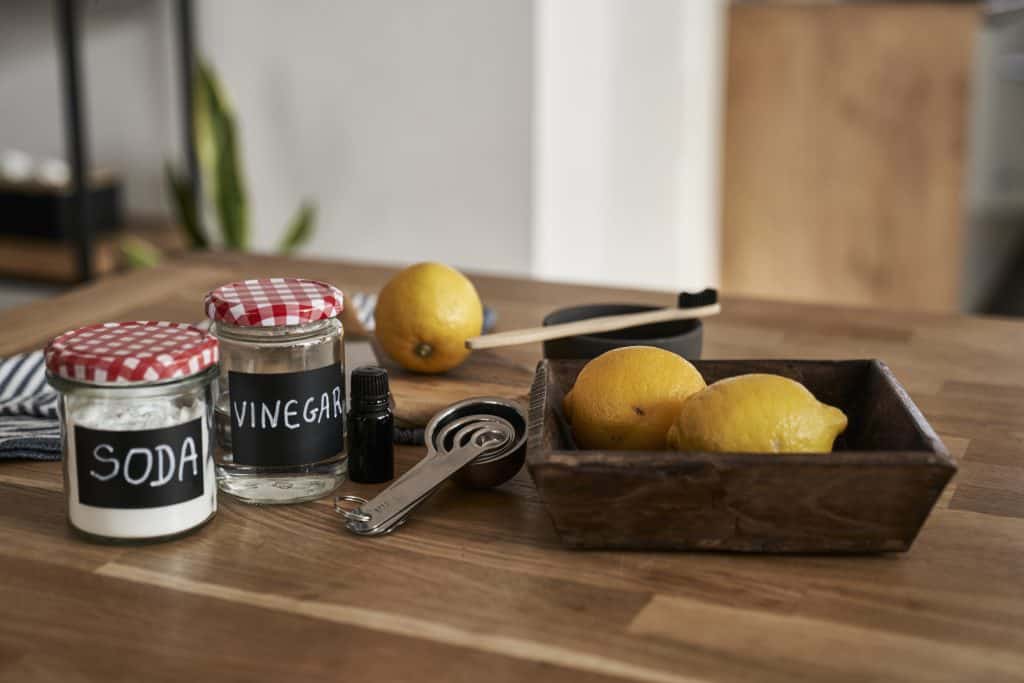 Soda and vinegar cleaning supplies on wooden table with lemons and measuring tools.