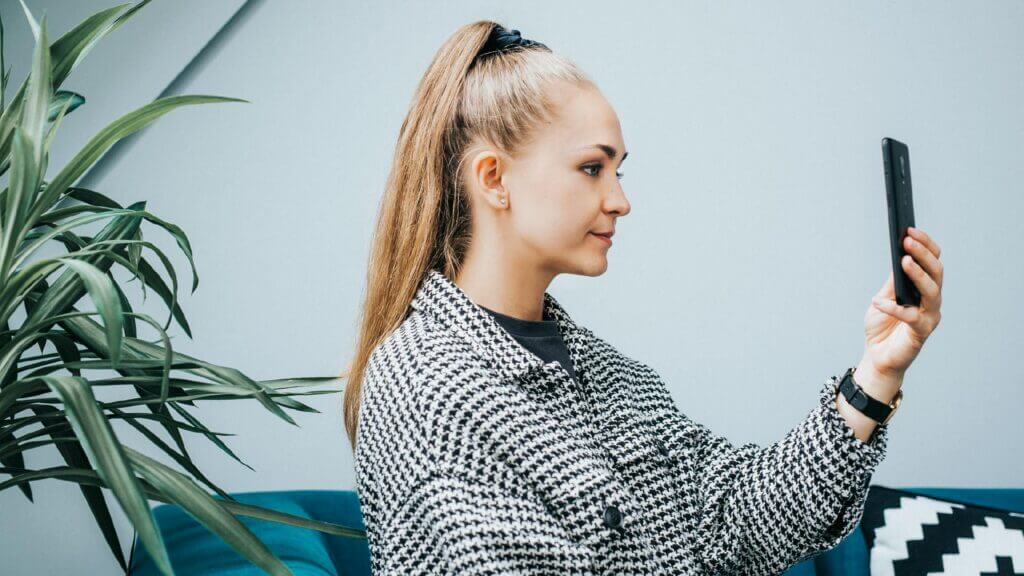 A girl sat down taking a selfie on a smart phone.