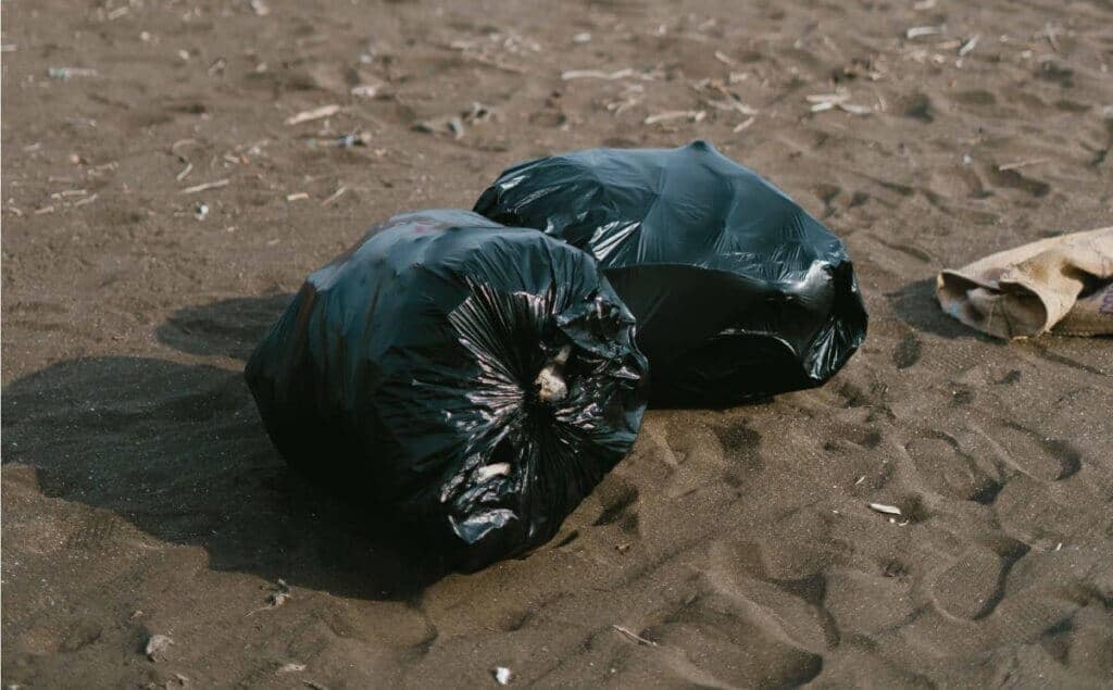 Sacolas de lixo pretas cheias na praia de areia.
