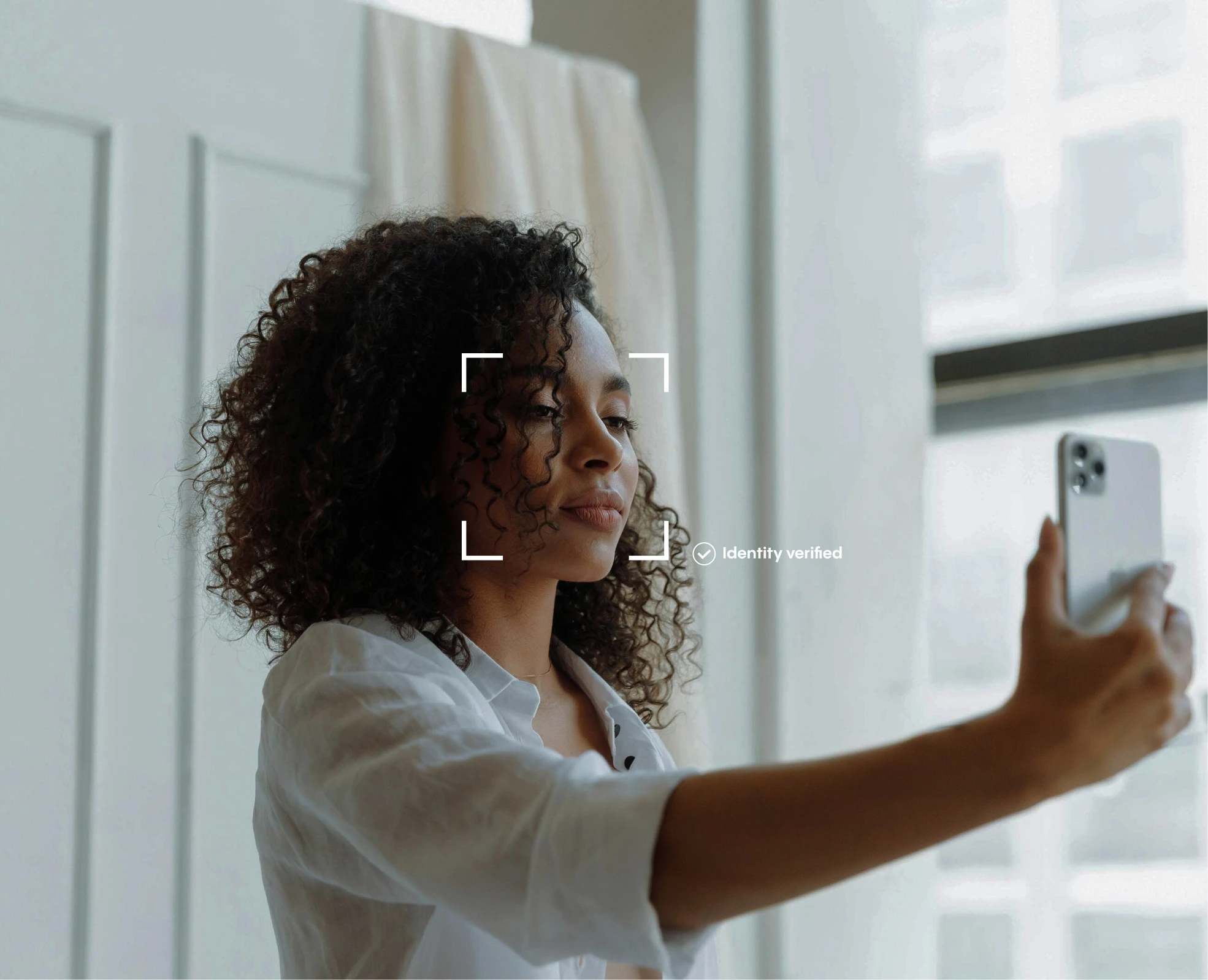 A woman smiling as she takes a selfie with her smartphone for an identity verification