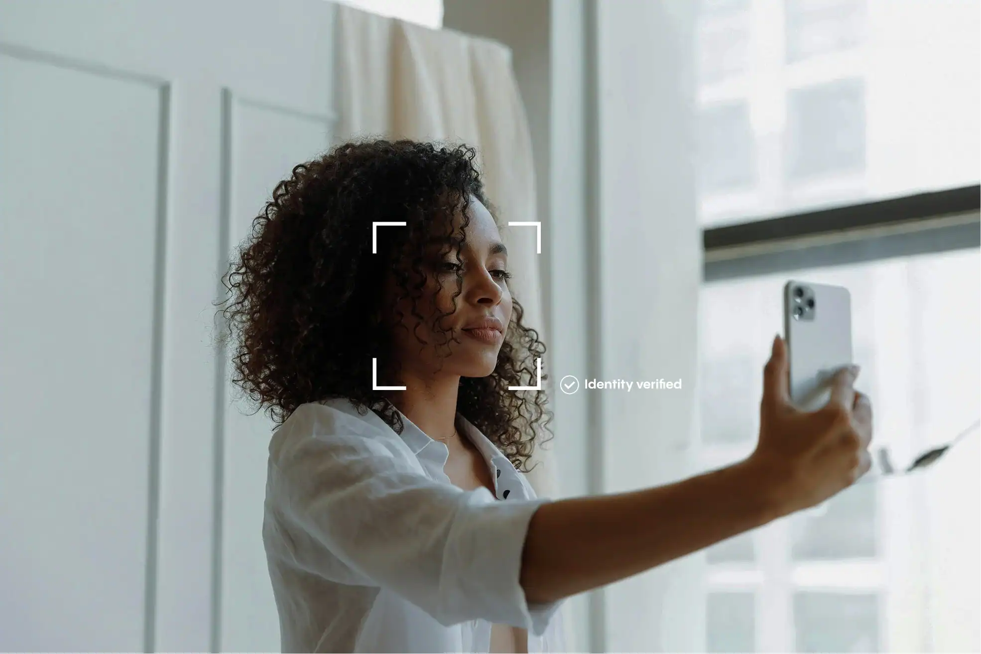 A woman smiling as she takes a selfie with her smartphone for an identity verification