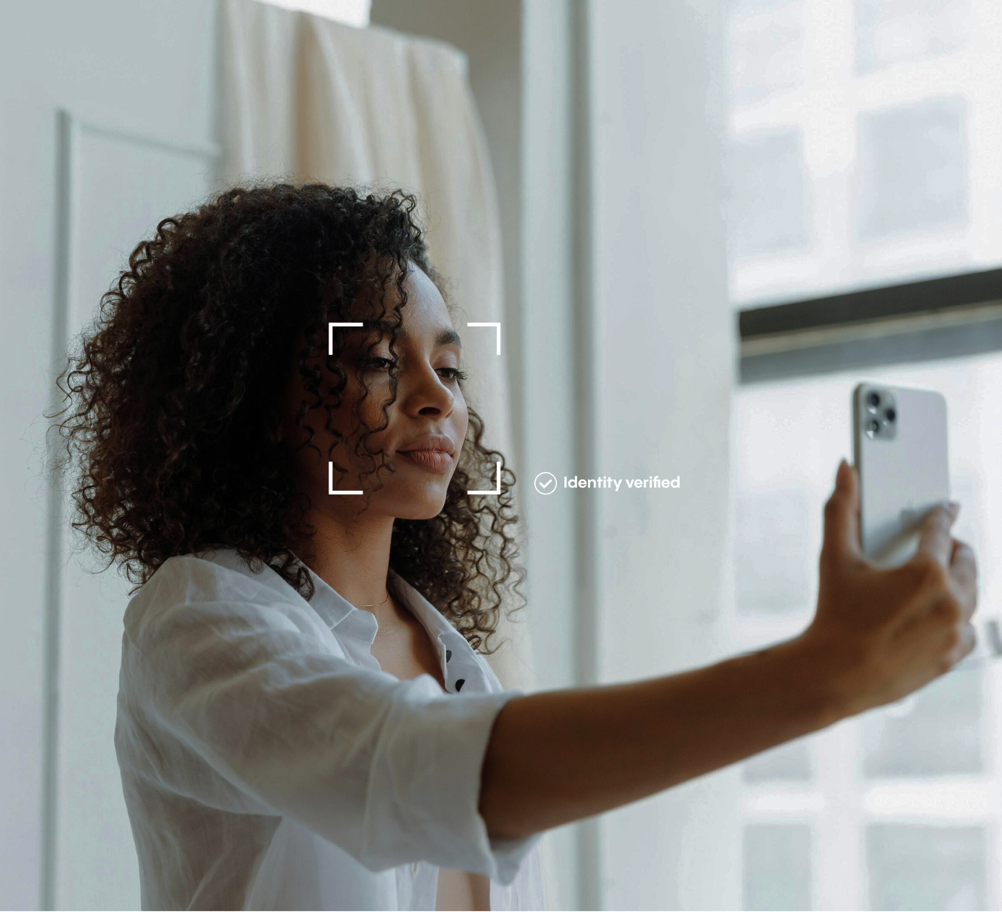 A woman smiling as she takes a selfie with her smartphone for an identity verification