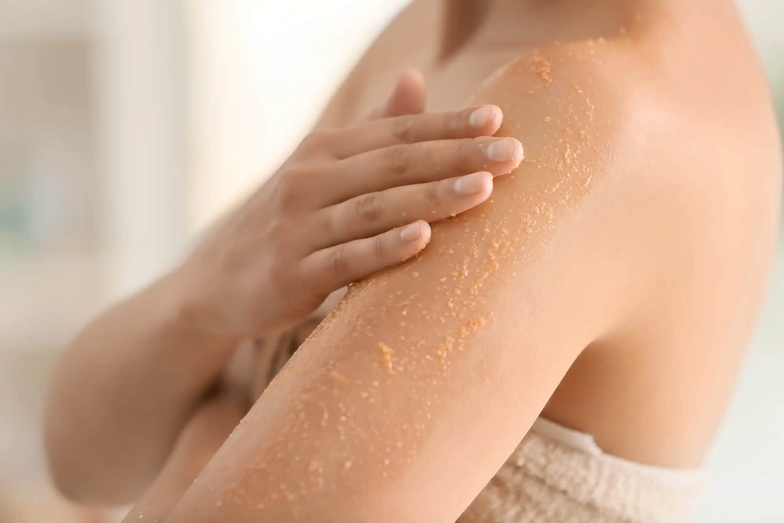 Woman uses a body scrub to exfoliate the skin on her arm