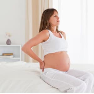 Beautiful pregnant female having a back pain while sitting on a bed in her apartment