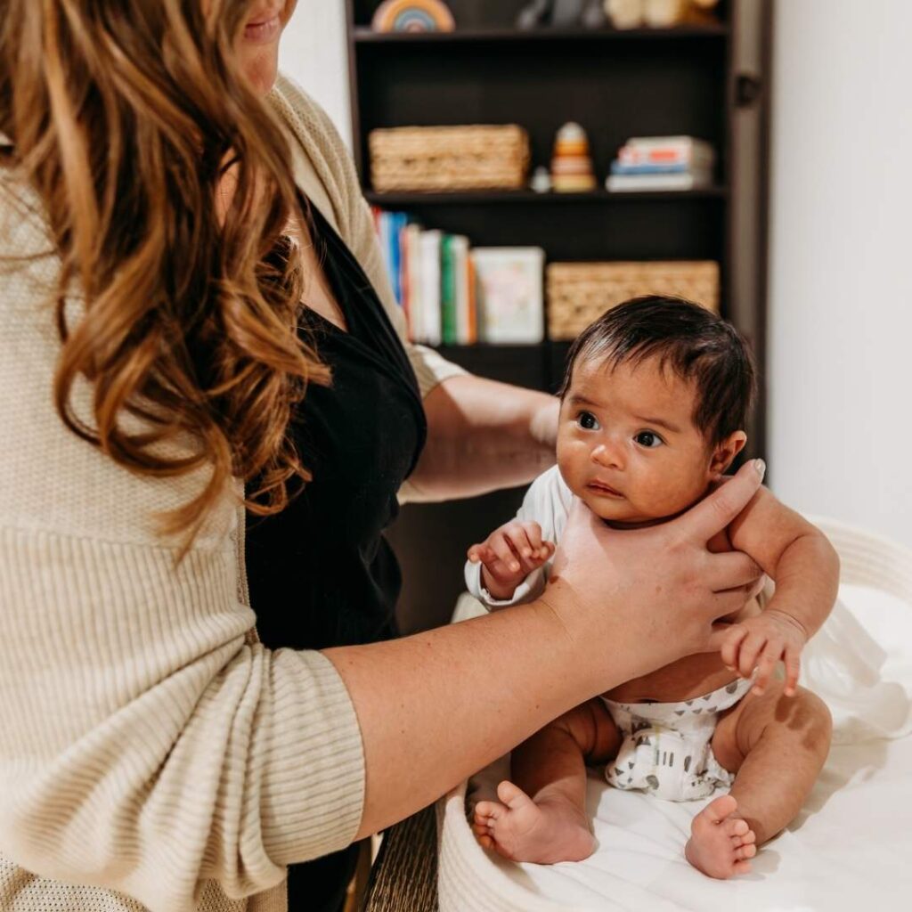 Newborn care specialist sitting a baby up and changing their clothes