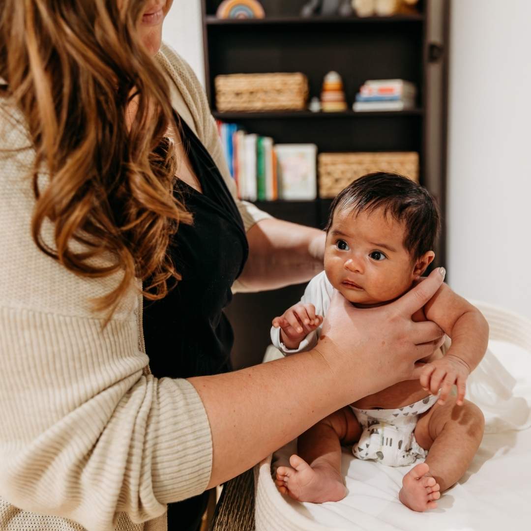 Newborn care specialist sitting a baby up and changing their clothes