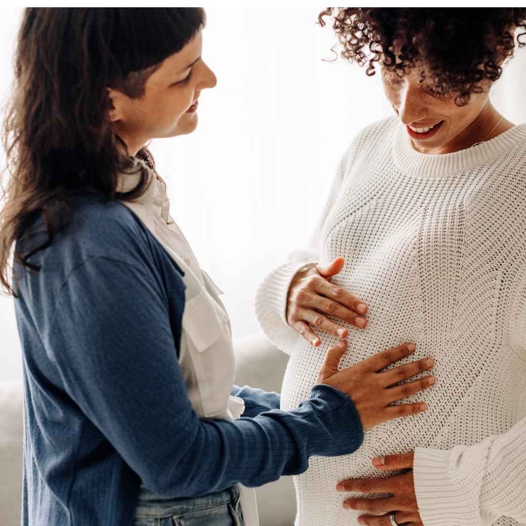 pregnant woman in a white sweater and another person with a hand on their belly
