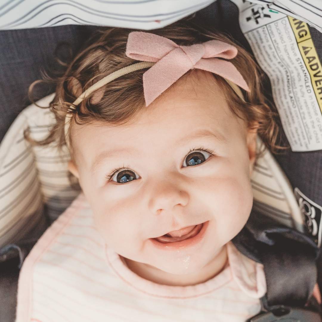 baby smiling in a carseat with a pink bow headband