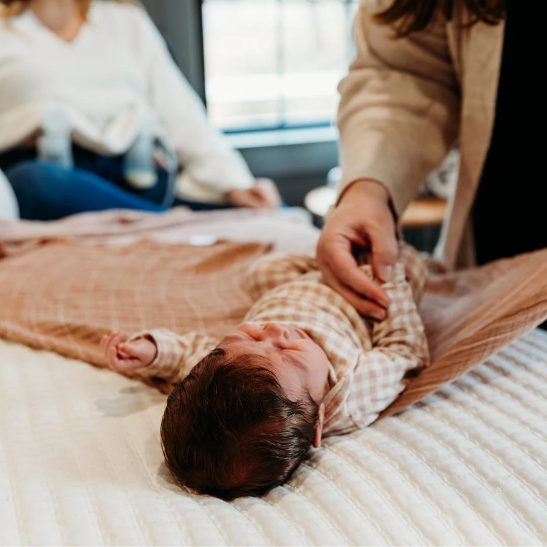 fussing baby being swaddled on a bed with a brown swaddle
