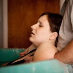 laboring mother in a birth tub with her partner behind her