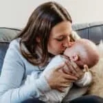 mom holding and kissing her swaddled baby