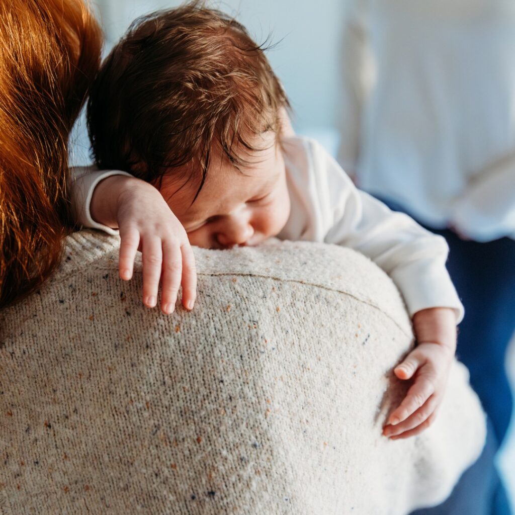 newborn sleeping baby draped over the shoulder of a newborn care specialist