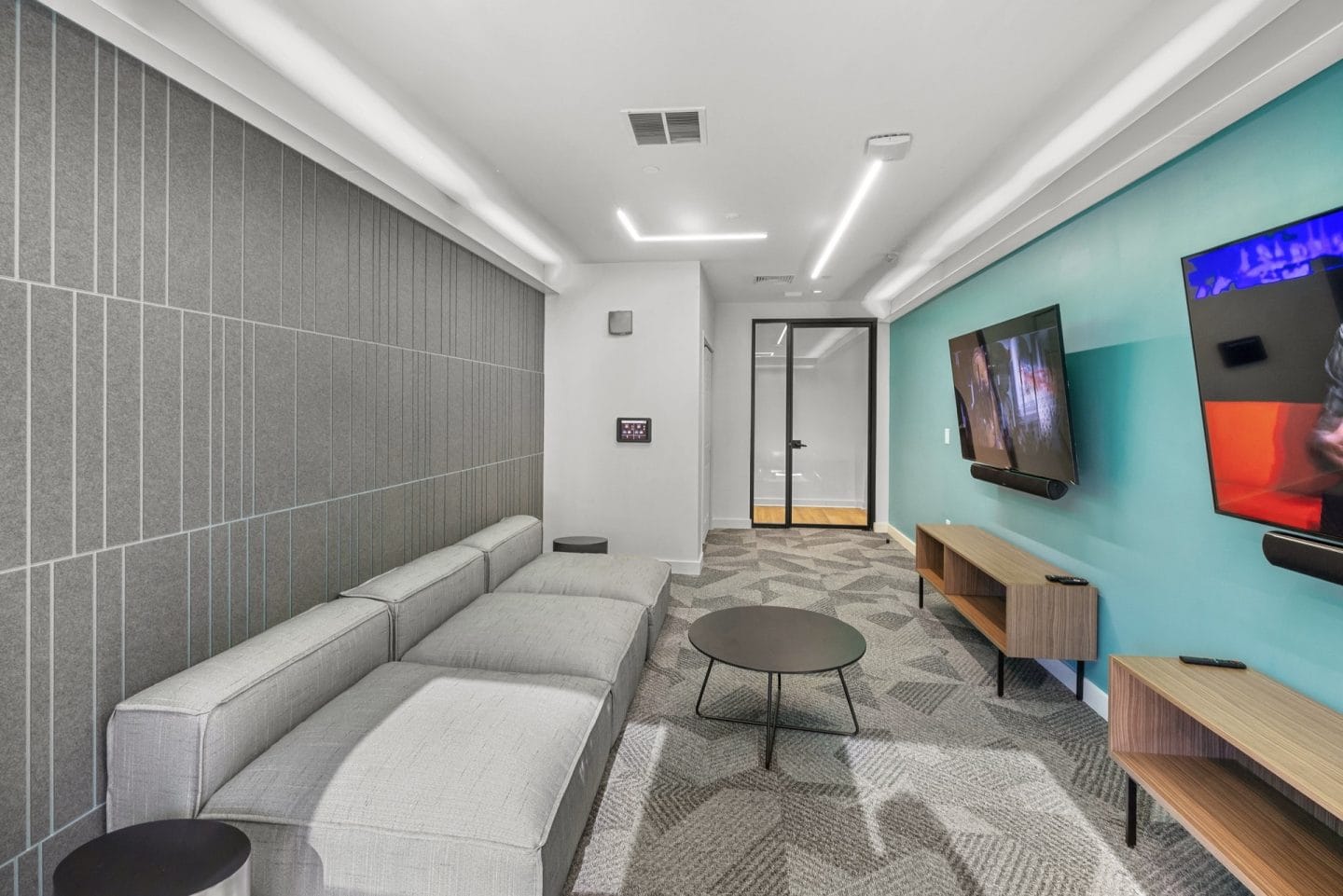 A modern waiting room with a grey sofa, a round table, and a TV mounted on the wall.