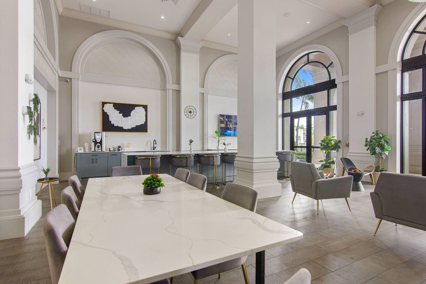 A large white table is surrounded by grey chairs in a spacious room with arched windows.