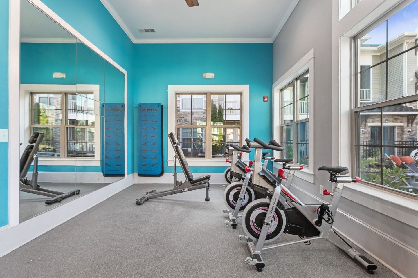 Spin and yoga studio at Windsor Sugarloaf 1455 Satellite Blvd Suwanee GA 30024 with stationary bikes mirrors blue accent wall and natural light offering space for cycling stretching or low impact movement