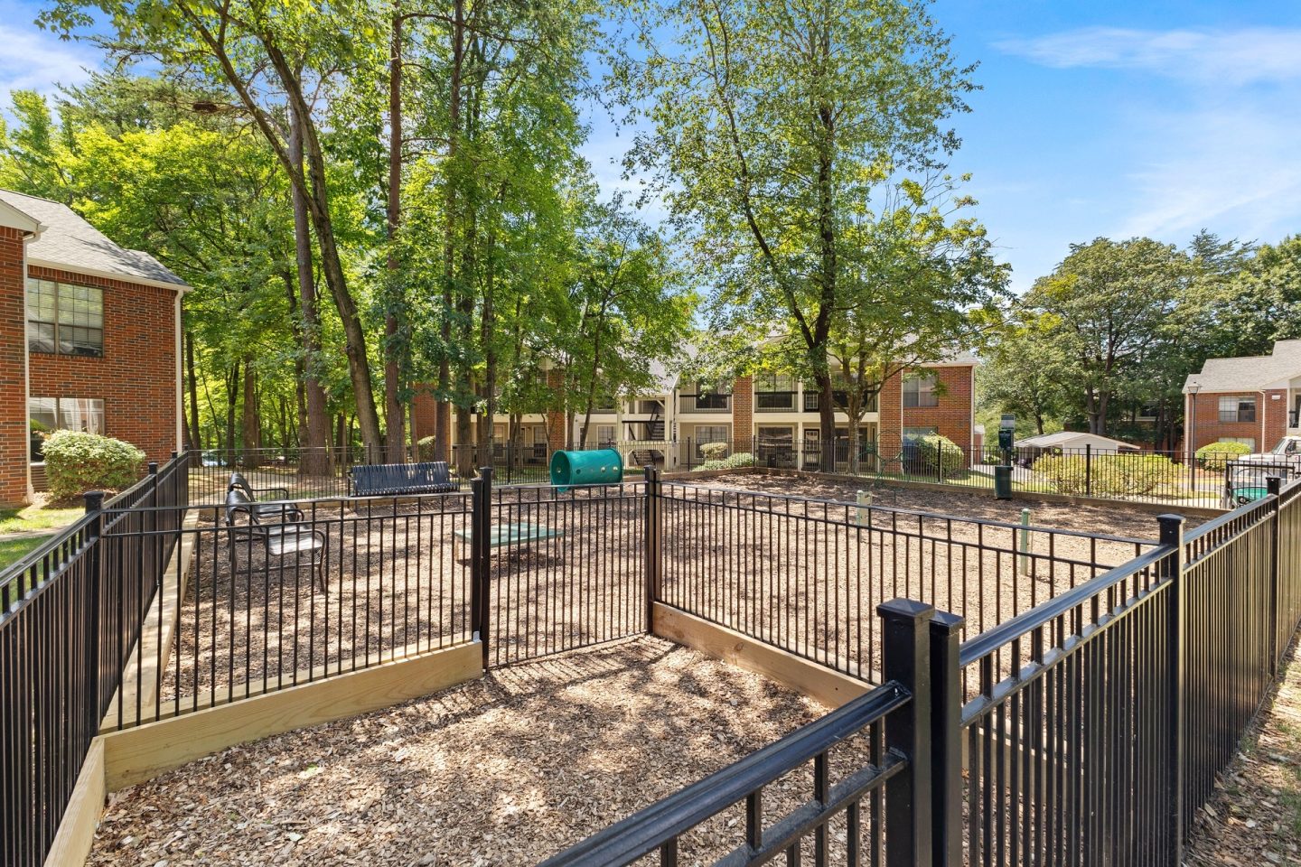 A playground surrounded by a black fence with a green slide.