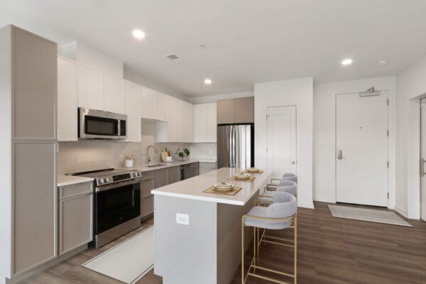 Modern Windsor Leesburg kitchen with light cabinets, stainless steel appliances, an island with seating for four, and wood flooring. The space is bright with neutral tones and minimalist decor.