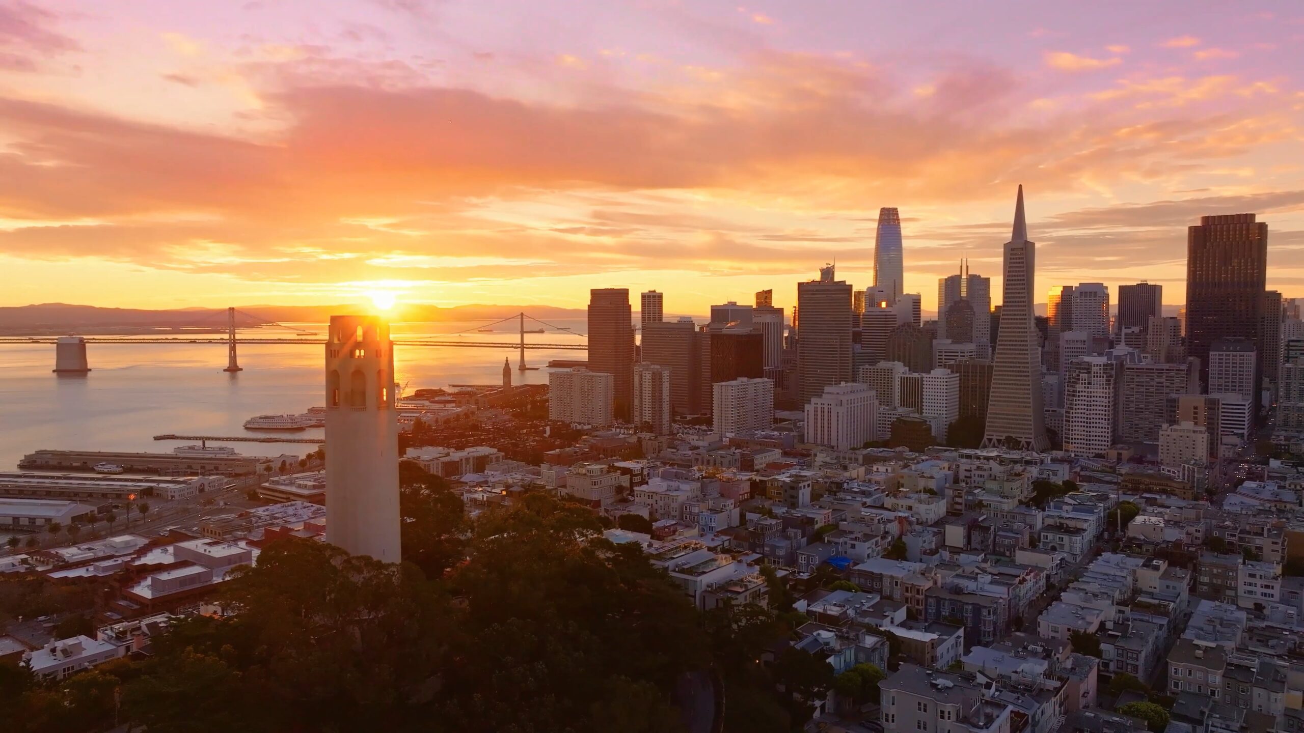 Aerial view of San Francisco, California at sunset with Coit Tower, downtown skyline, and the Bay Bridge