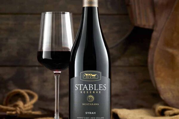 A bottle of Stables red wine and a glass on a wooden table.