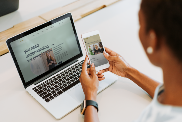 A woman is using her phone to look at the Sapere website on a laptop.