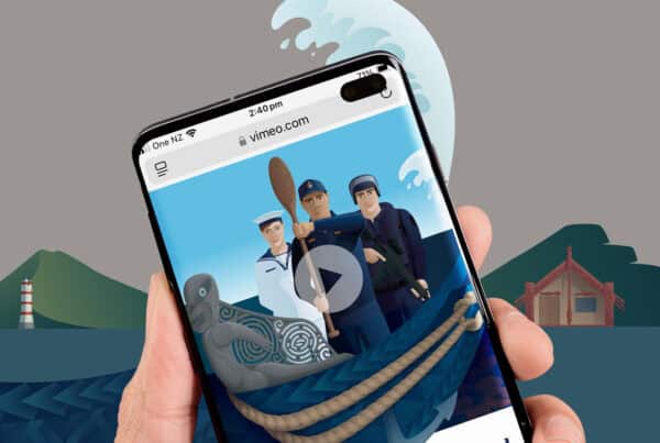 A hand holding a smartphone displaying an illustration of three sailors in an animated video on vimeo.com. The background shows a large wave, a lighthouse, and green hills. A carved grey figurehead of a waka and rope are visible at the bottom of the phone screen.
