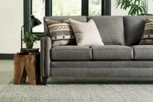 A contemporary gray sofa with plush cushions and decorative pillows, placed in a well-lit living room. Perfect for showcasing furniture brands that last generations, emphasizing quality and style.