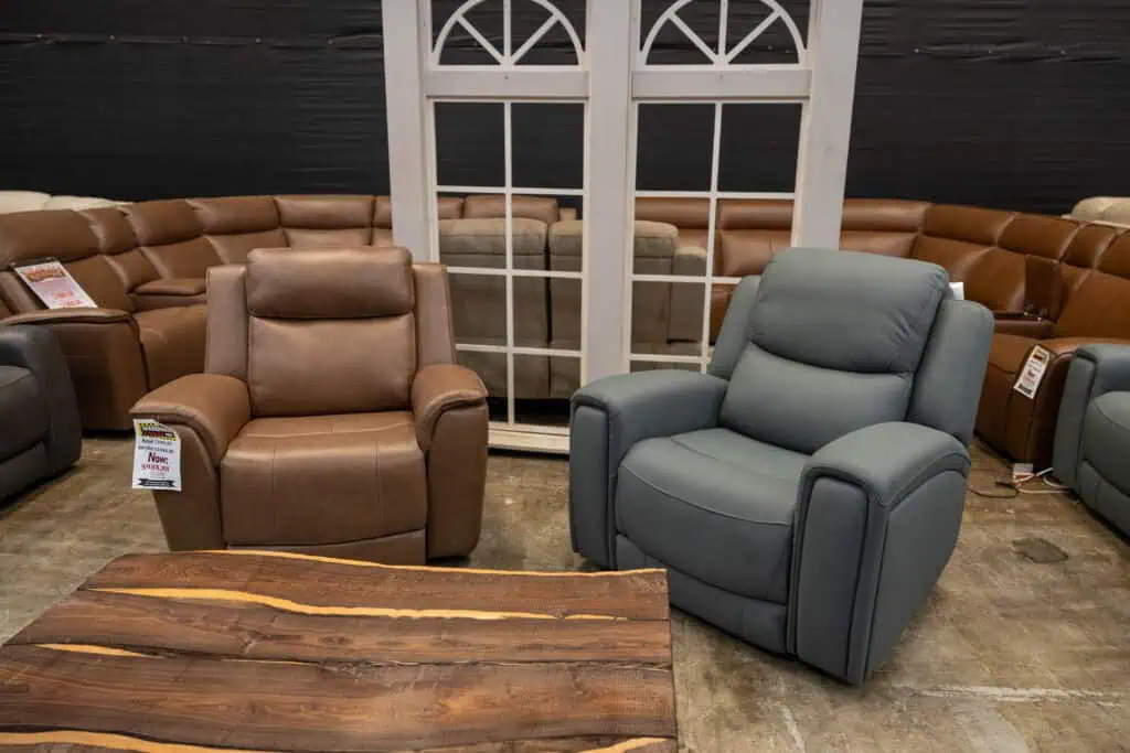 Two leather recliner chairs, one brown and one gray, in a furniture store.
