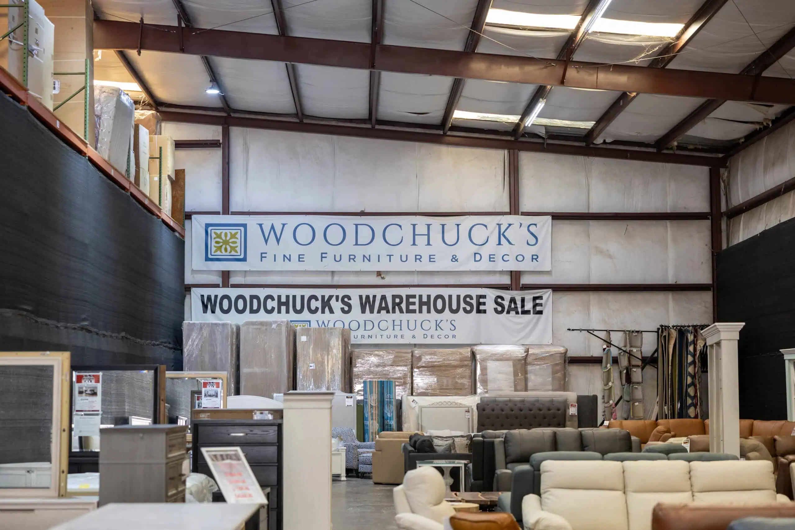 Interior of a warehouse with furniture and signs for Woodchuck's Warehouse Sale.