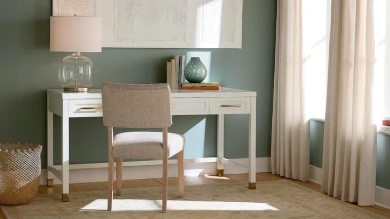 An office set up with a white desk, neutral chair, and decorative pieces.