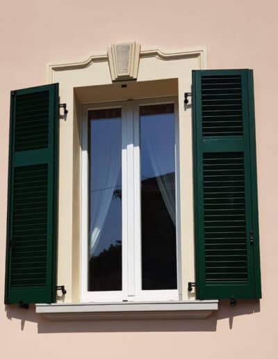 Finestra con persiane in legno verde su parete chiara, stile classico e raffinato.
